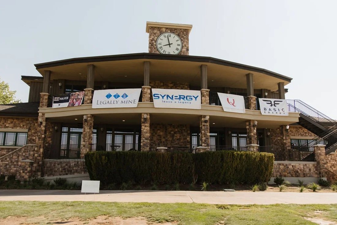 Sponsor banners on the tournament clubhouse balcony: a Legally Mine banner next to a Synergy banner
