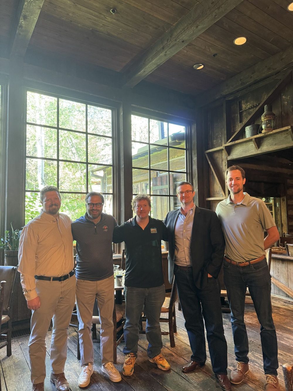 Five men standing together in a rustic wood-paneled restaurant. From left: Ammon McNeff, Jonathan Hill, and Matthew McNeff in a Bricks and Minifigs logo shirt, with two others, from the Utah Franchise Family post.