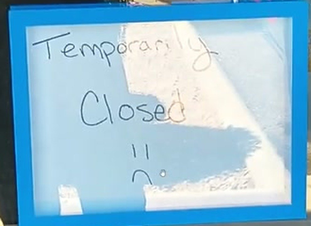 A whiteboard in a blue frame taped inside the store's glass door. Handwritten on it: Temporarily Closed, with a sad face drawn underneath.