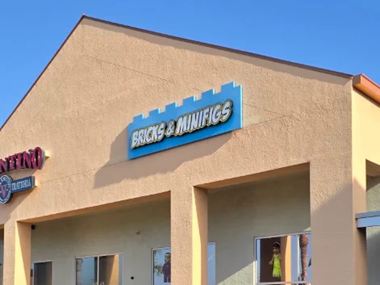 The gable of the store at 4047 Clark Rd carrying the Bricks and Minifigs channel-letter sign, blue with a brick-shaped top edge.