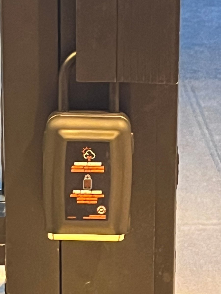A grey key lockbox padlocked through the pull handle of a dark storefront door, photographed after dark.