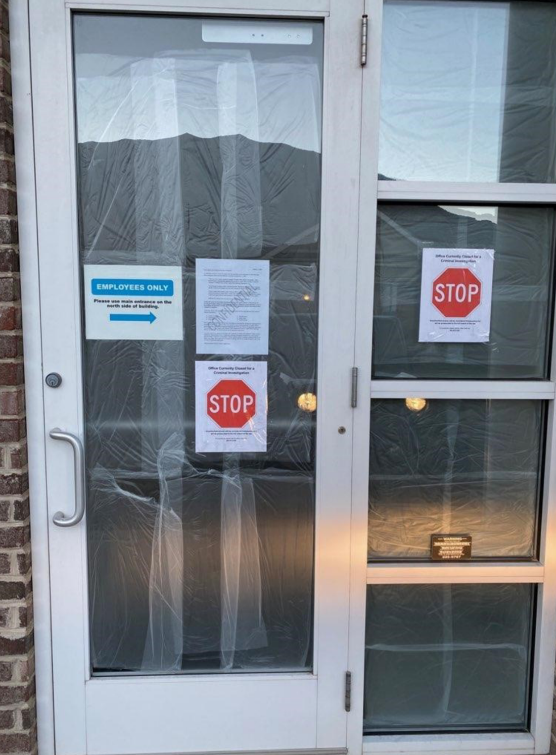 The glass entry door of Legally Mine's Orem office, the glass covered in plastic sheeting from inside, with an Employees Only sign, a posted notice marked Confidential, and two printed signs each carrying a red STOP octagon under the words Office Currently Closed for a Criminal Investigation
